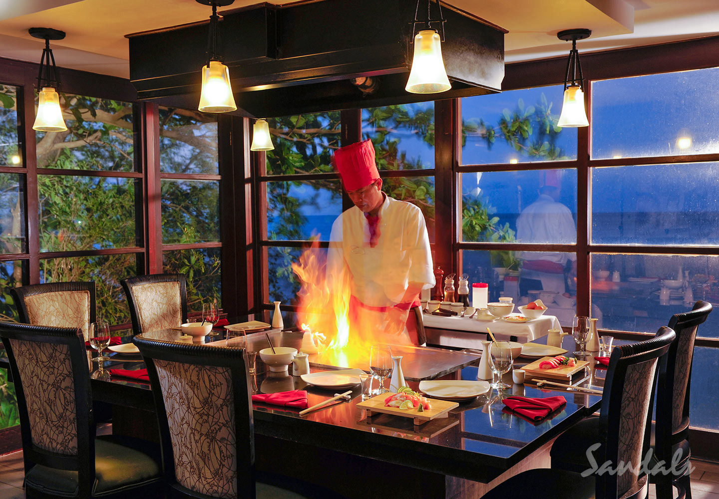 A teppanyaki chef preparing dinner at a candlelit table beside the sea at dusk