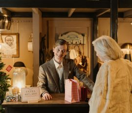 Europe A cheerful shopkeeper assists a customer during a festive sale event in a cozy store setting.