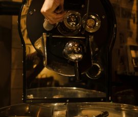 Europe A close-up view of a hand adjusting a coffee roaster machine indoors.